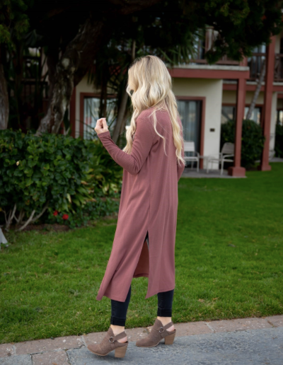 Woman in a long pink cardigan walking outdoors on a grassy area.