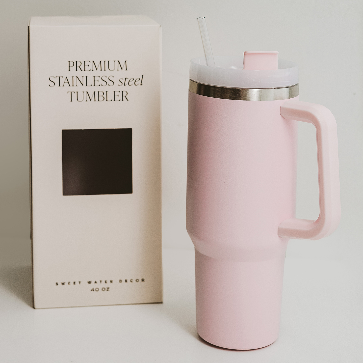 Pink stainless steel tumbler with handle next to its packaging on a light gray background