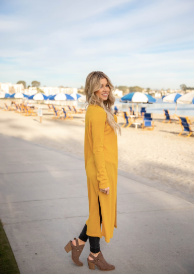 Woman in a yellow long coat standing on a paved area with a scenic background.