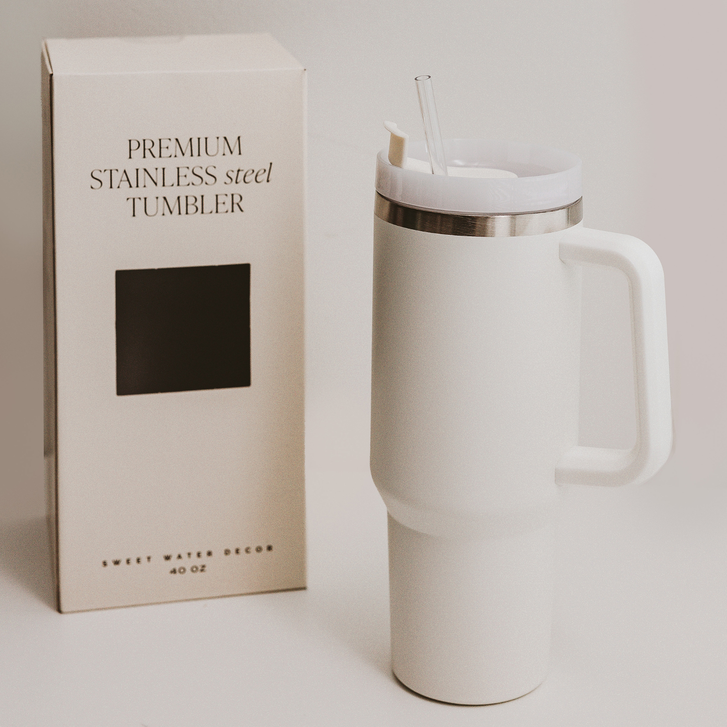 White stainless steel tumbler with handle and straw next to its packaging on a light background