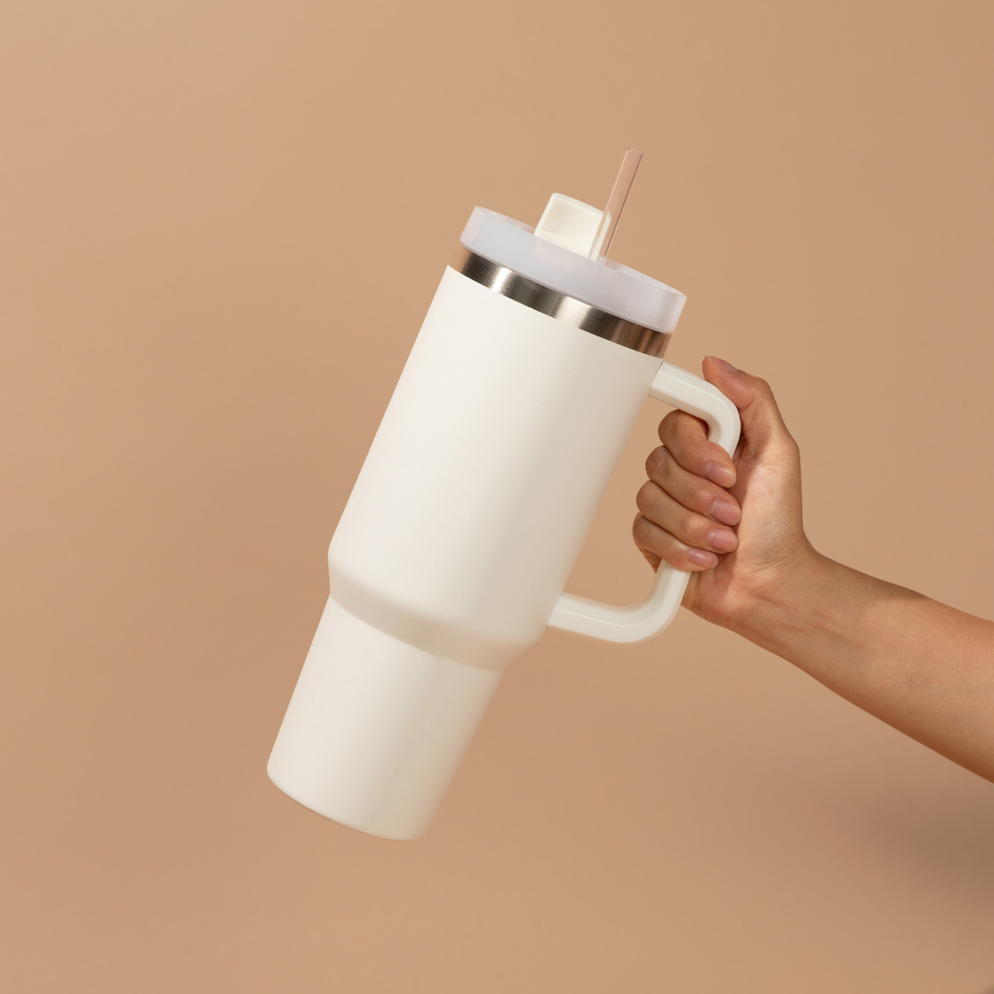 White insulated tumbler with a handle held by a hand against a beige background