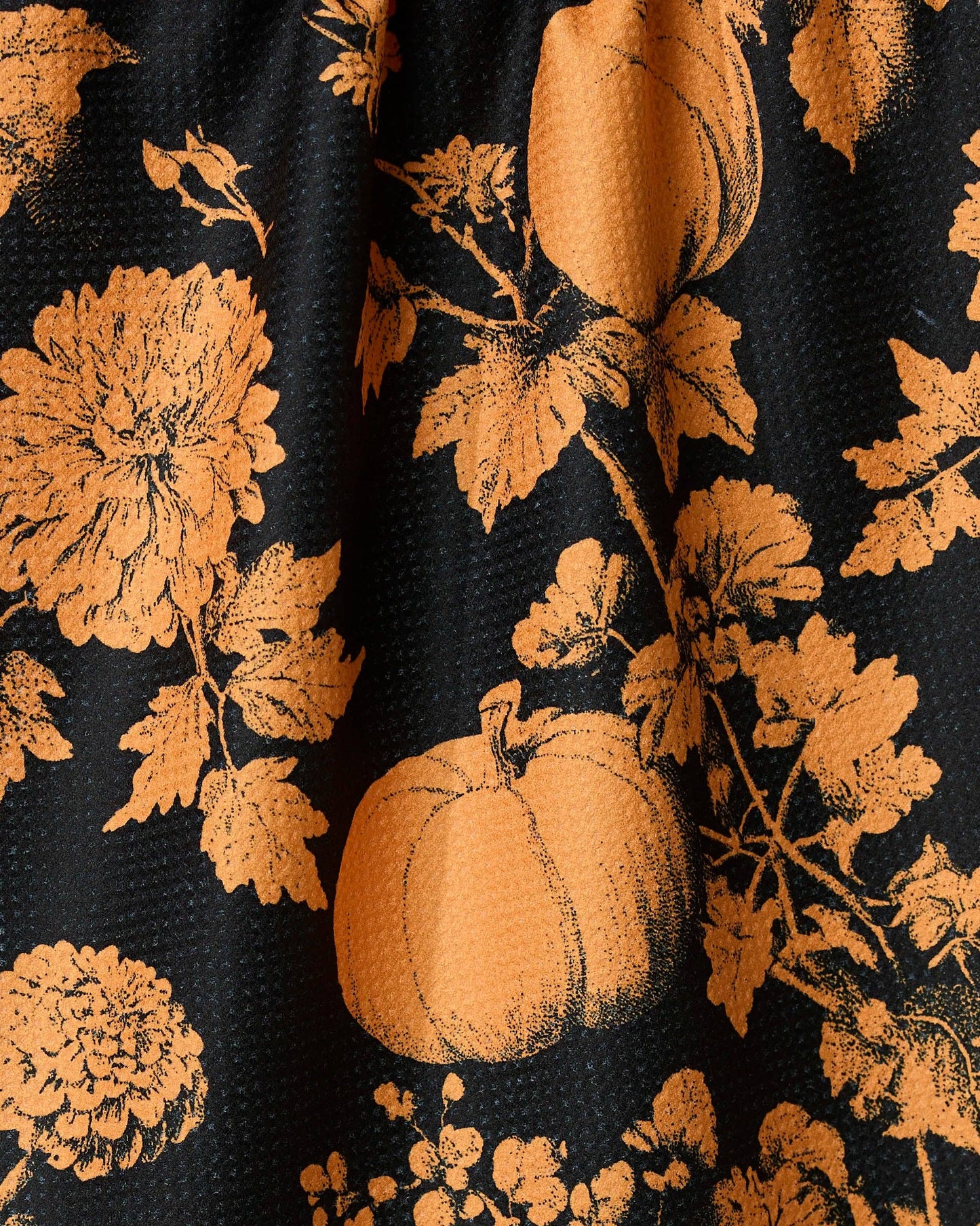 Black Geometry brand kitchen tea towel with orange floral and pumpkin pattern on a beige background