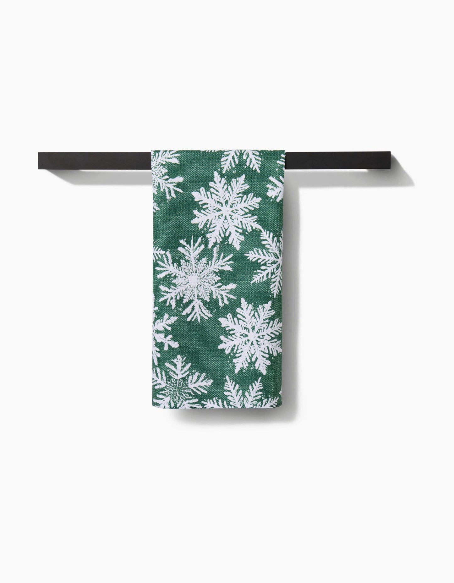 Green towel with white snowflake pattern hanging on a black metal rack against a white background