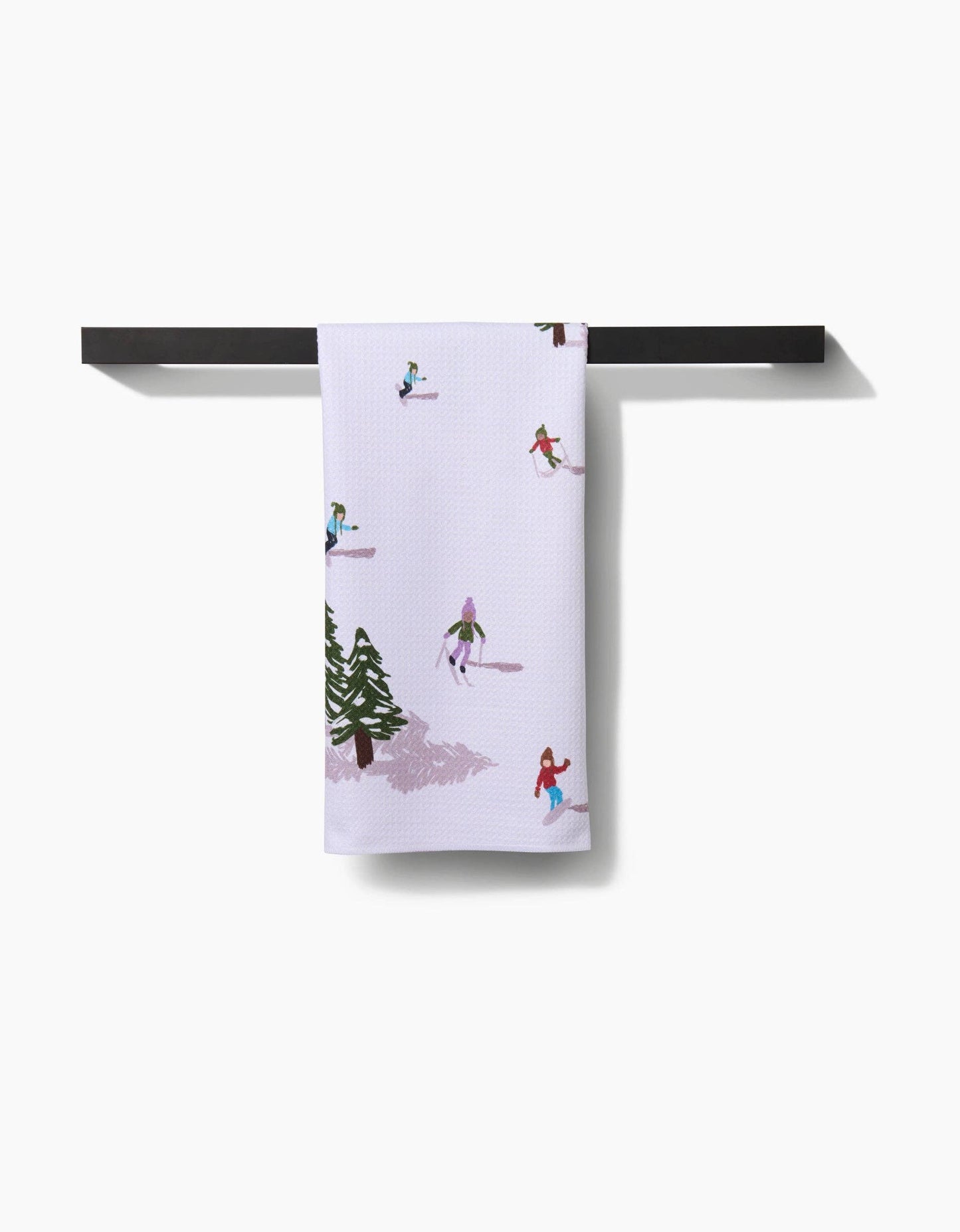 Towel with winter scene design hanging on a black rod against a white background