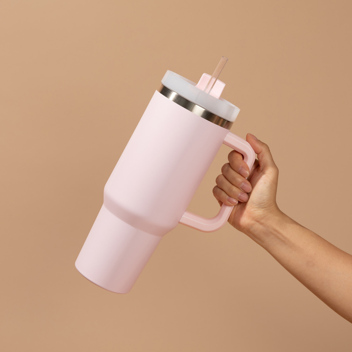 Pink insulated tumbler with a handle held by a hand against a beige background