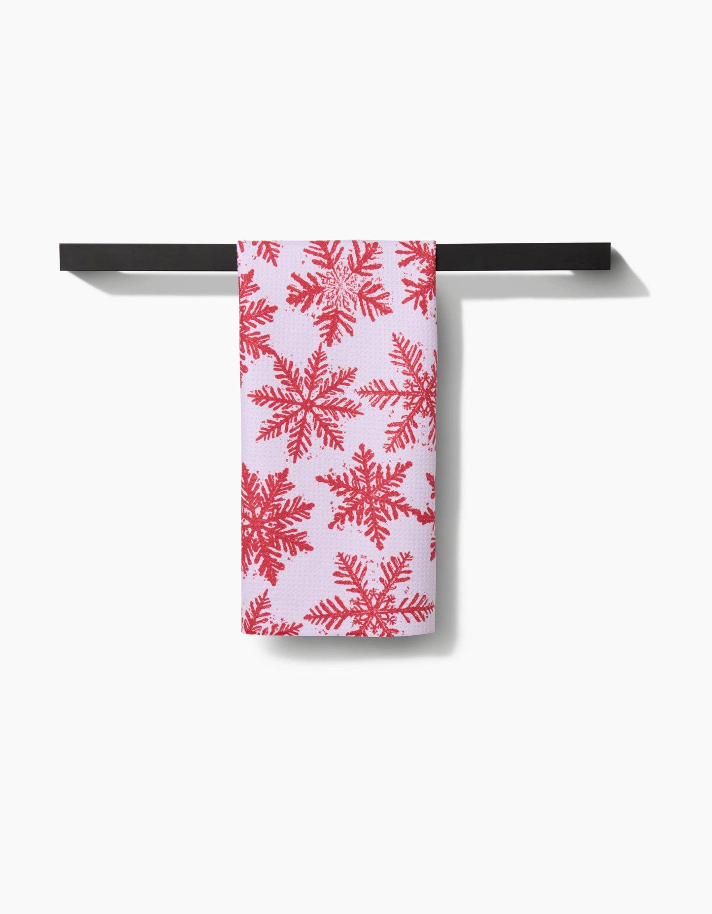 Towel with red snowflake pattern hanging on a black towel rack against a white background