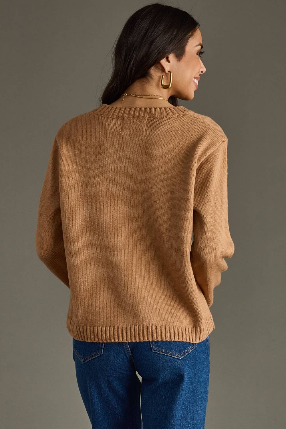 Woman wearing a brown sweater and blue jeans against a gray background