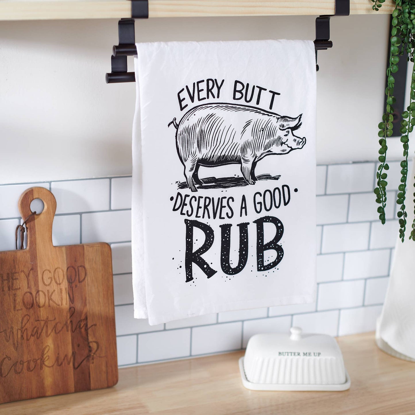 Kitchen towel with humorous design of a pig and text, hanging on a rack.