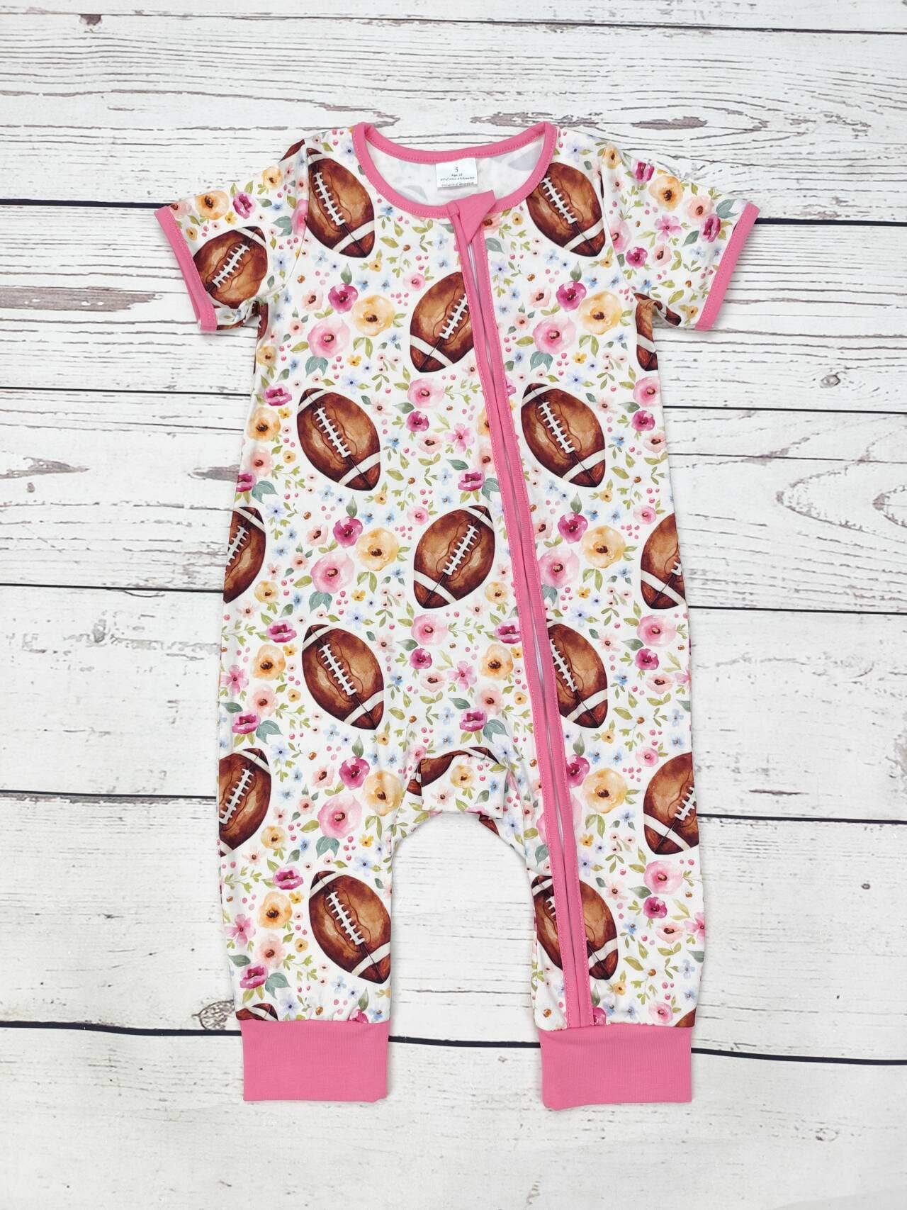 Baby romper with football and floral pattern on a wooden surface