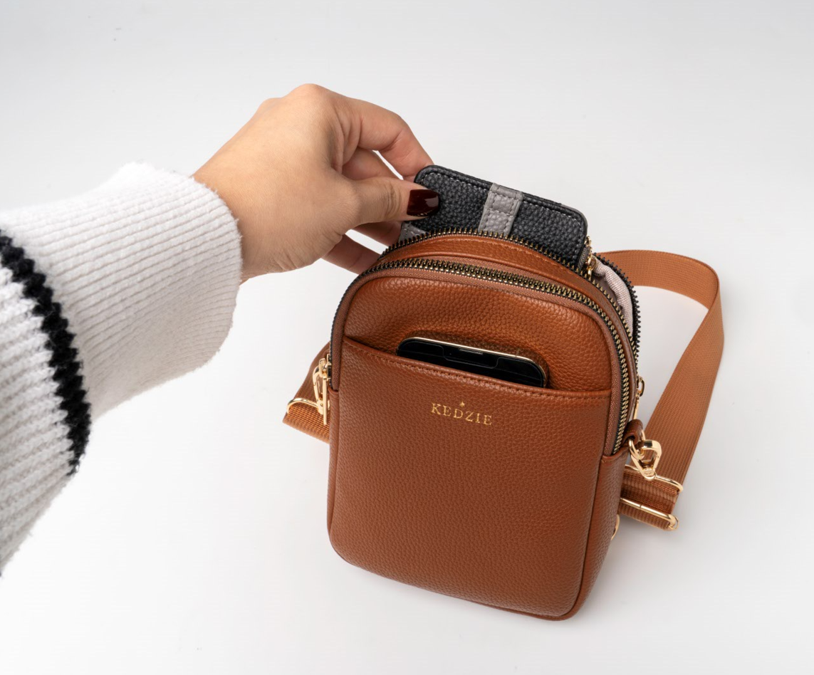 Brown crossbody bag with a hand pulling a zipper.