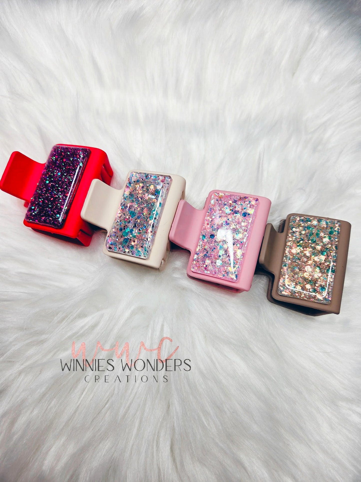 Four colorful hair clips with glittery design on a white fur background, branded 'Winnie's Wonders Creations'.