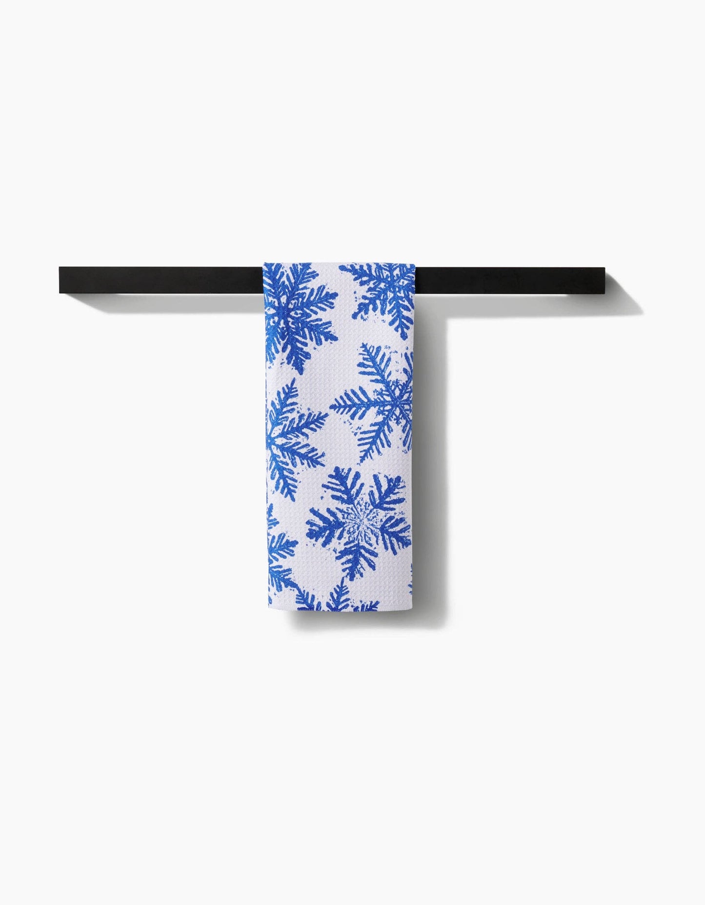 White towel with blue snowflake pattern hanging on a black rack against a white background