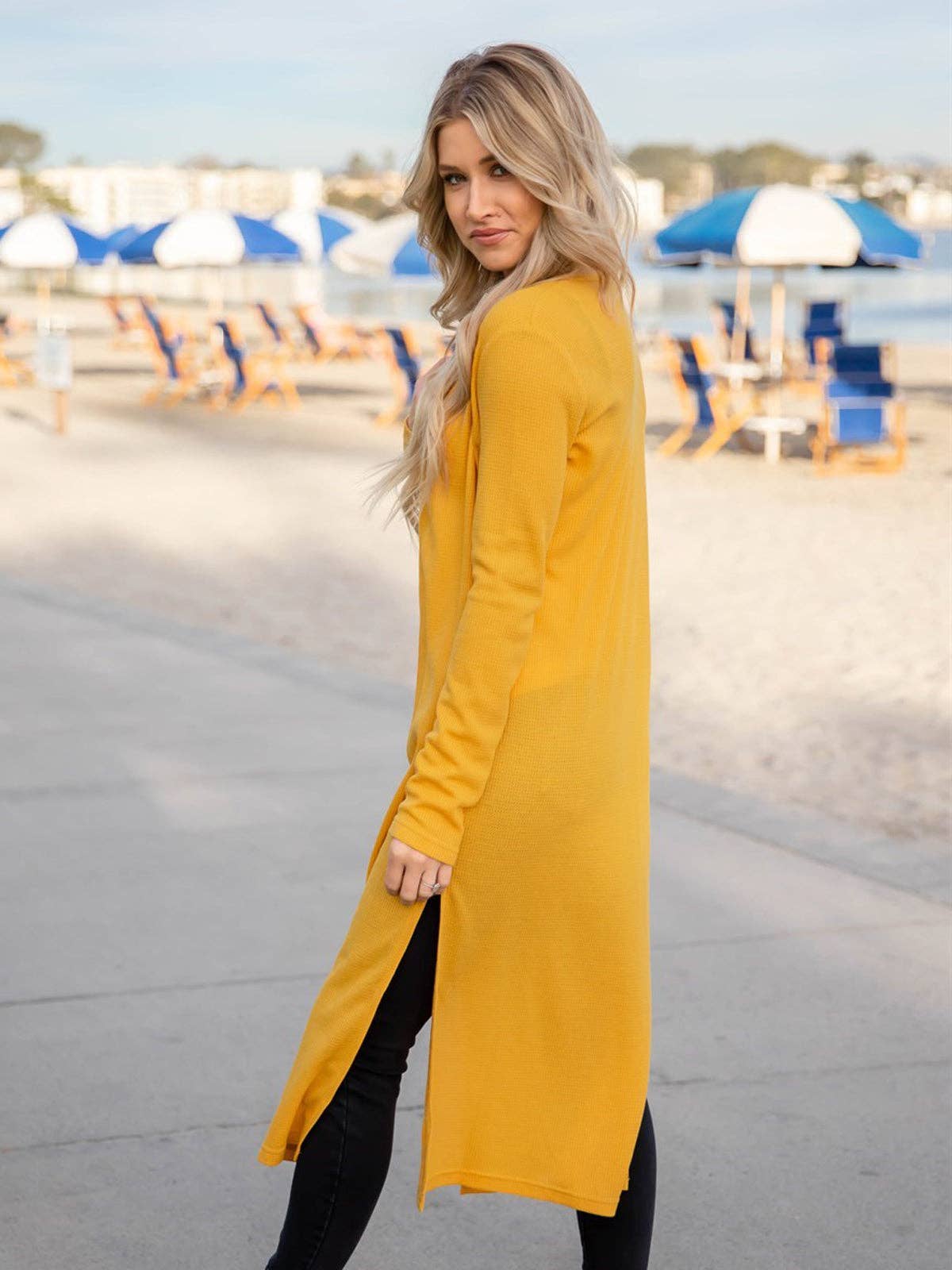 Woman wearing a long mustard yellow dress with a blurred beach background
