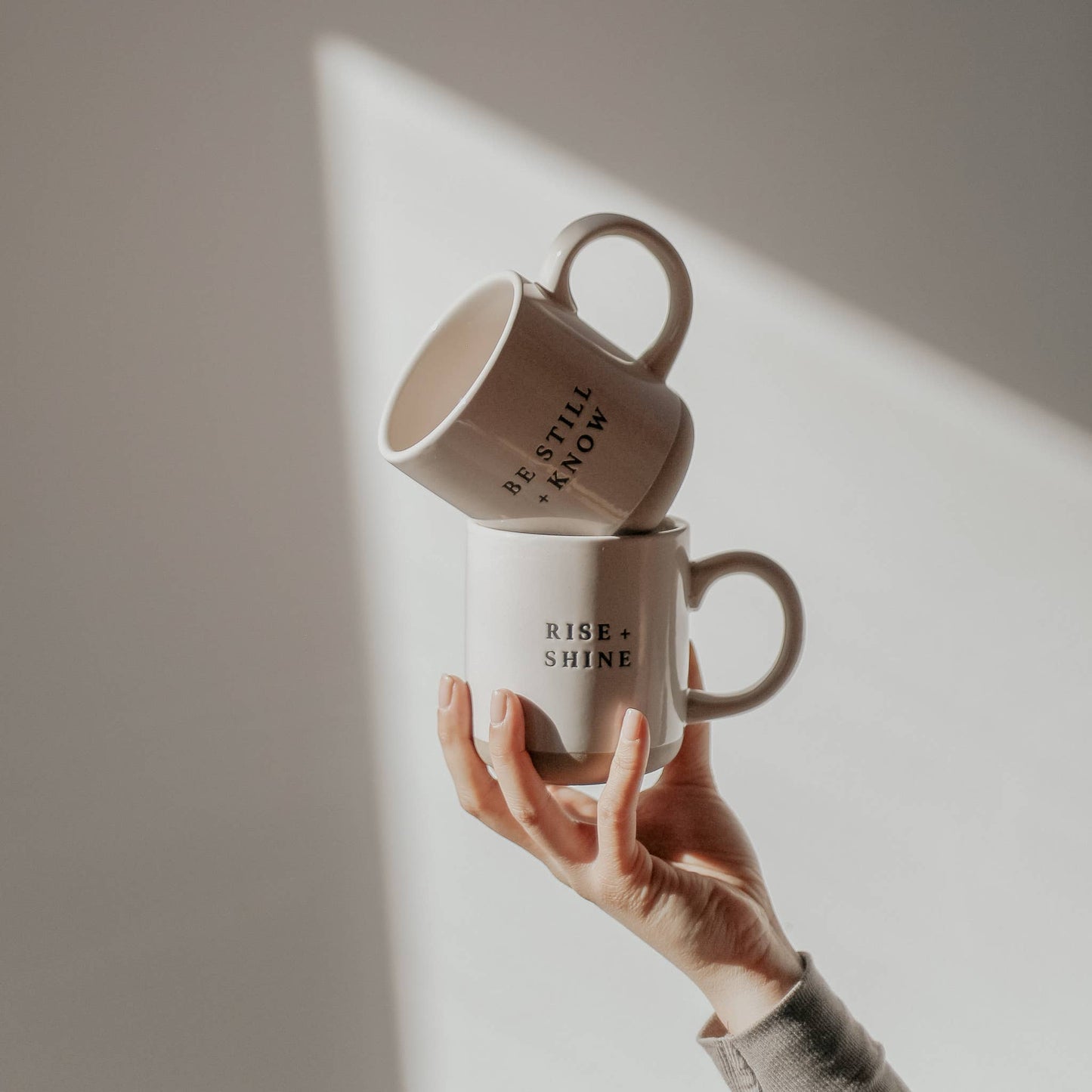 Two stacked mugs with motivational phrases held against a neutral background