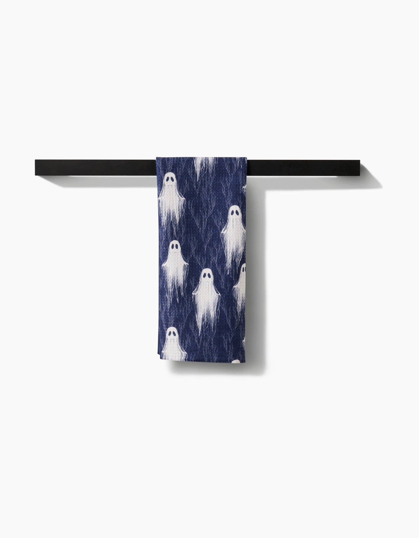 Navy blue towel with ghost pattern hanging on a black towel rack against a white background
