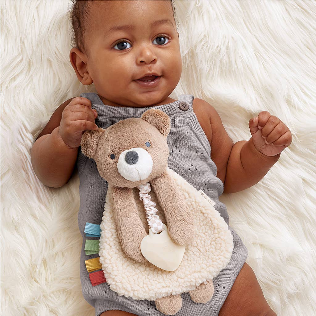 Baby in a gray outfit holding a teddy bear on a white fluffy surface