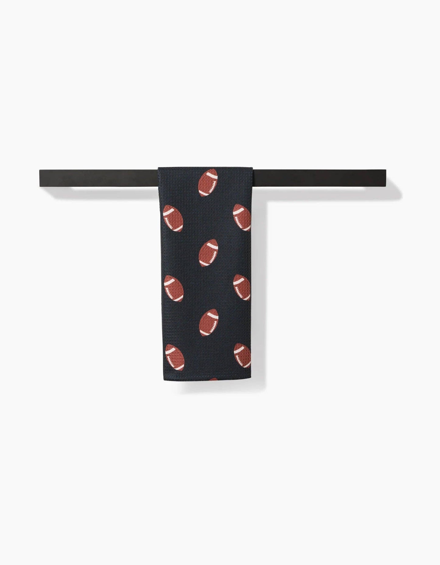 Black Geometry brand kitchen tea towel with brown football pattern on a white background hanging on a black towel bar