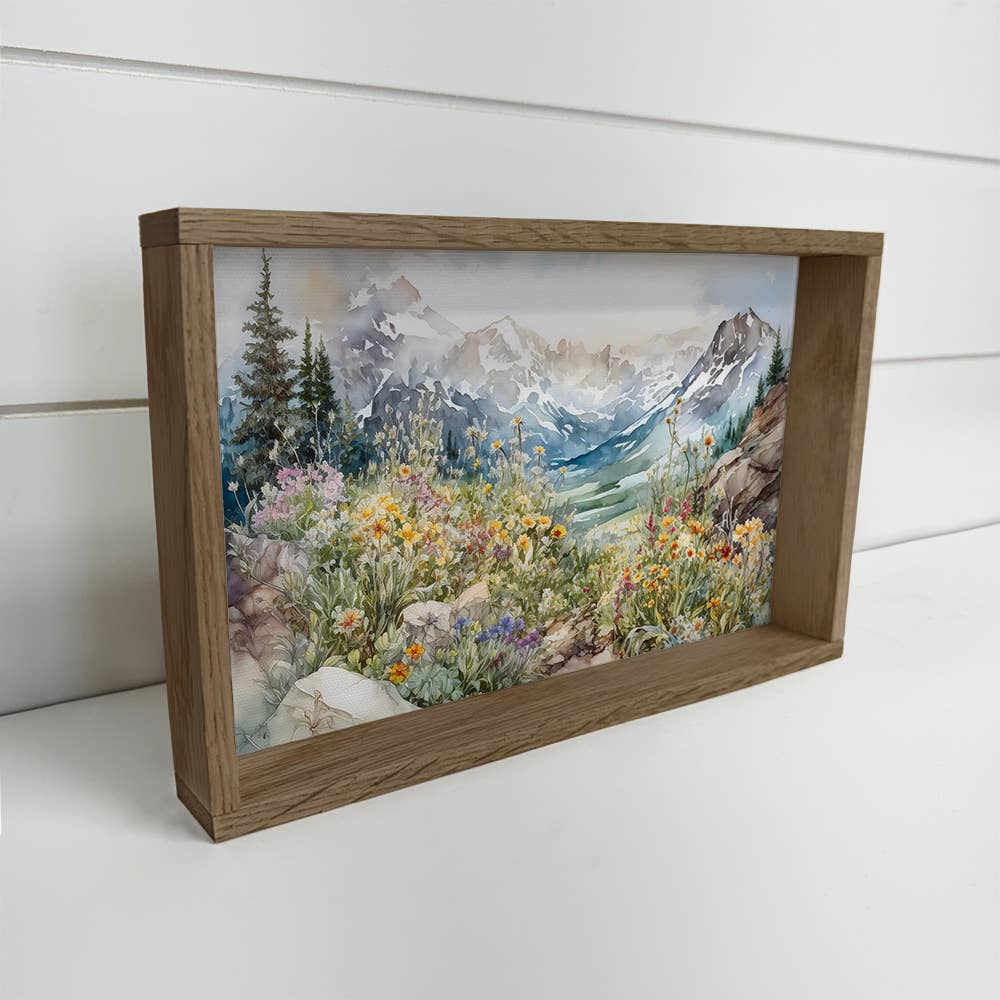 Framed artwork of a mountain landscape with flowers on a white surface.