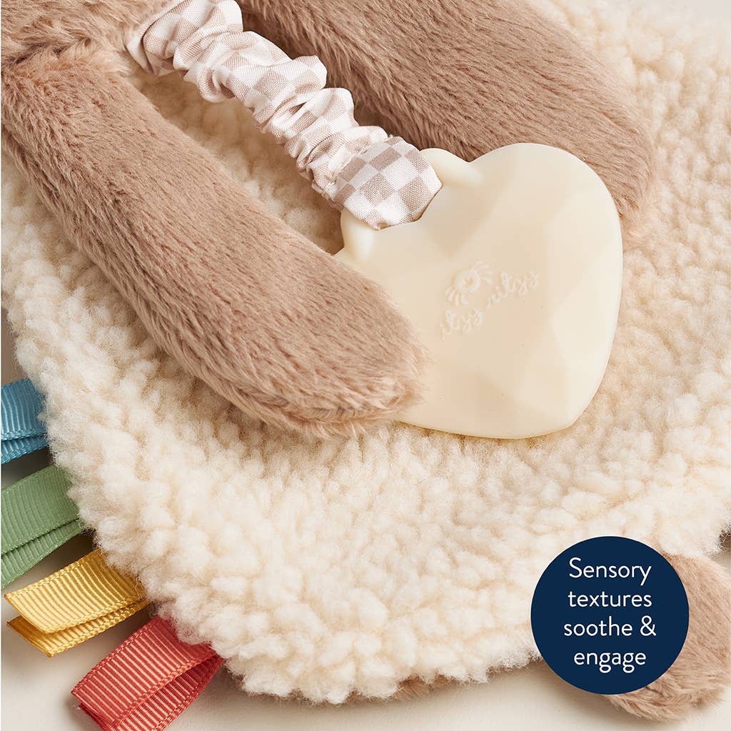 Heart-shaped toy with textured handle on a soft surface, featuring colorful ribbons.