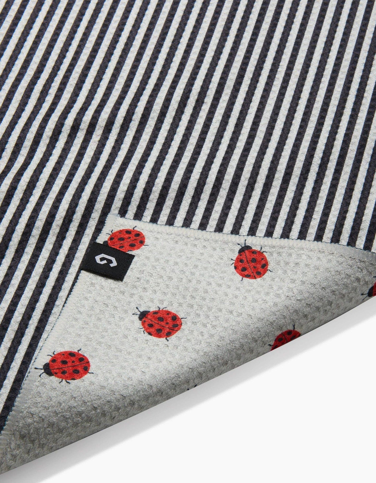 Textile with black and white striped pattern and red ladybug designs on a gray background