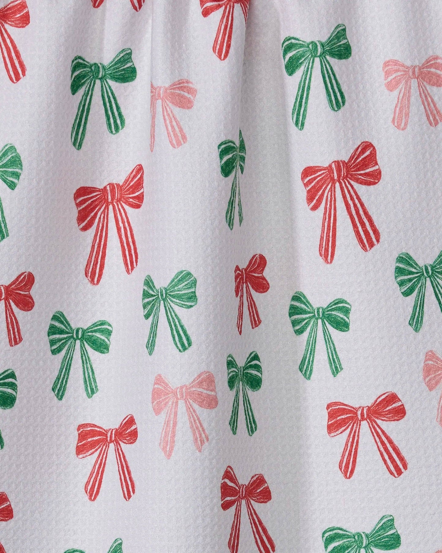 Geometry Tea Towel with red and green bow pattern hanging on a line against a green background
