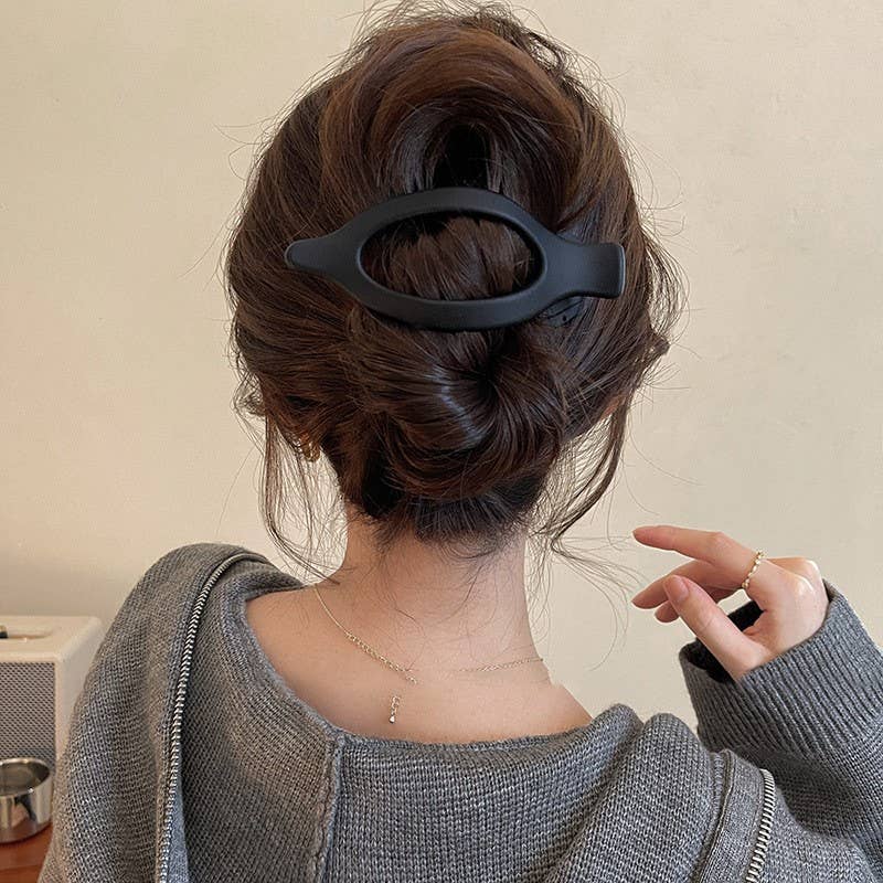 Person with a hair bun holding a black hair clip against a neutral background