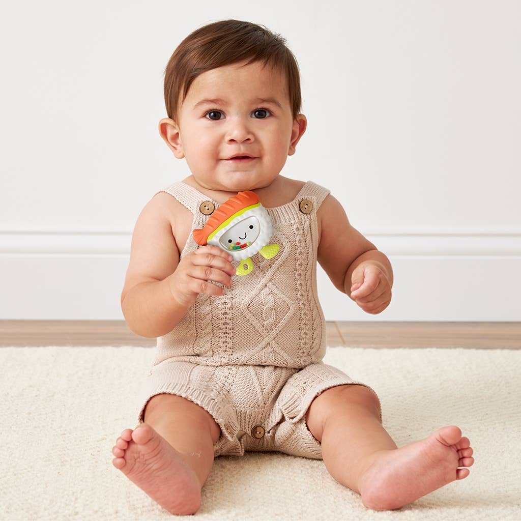 Baby in a knitted romper holding a colorful toy on a light background