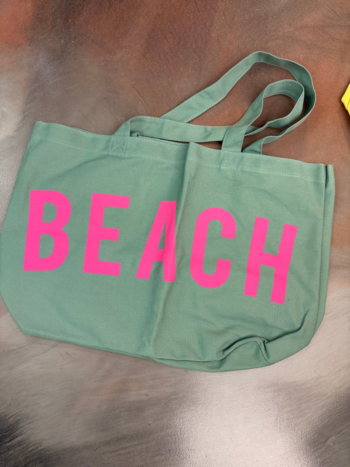 Green tote bag with 'BEACH' in pink letters on a wooden surface