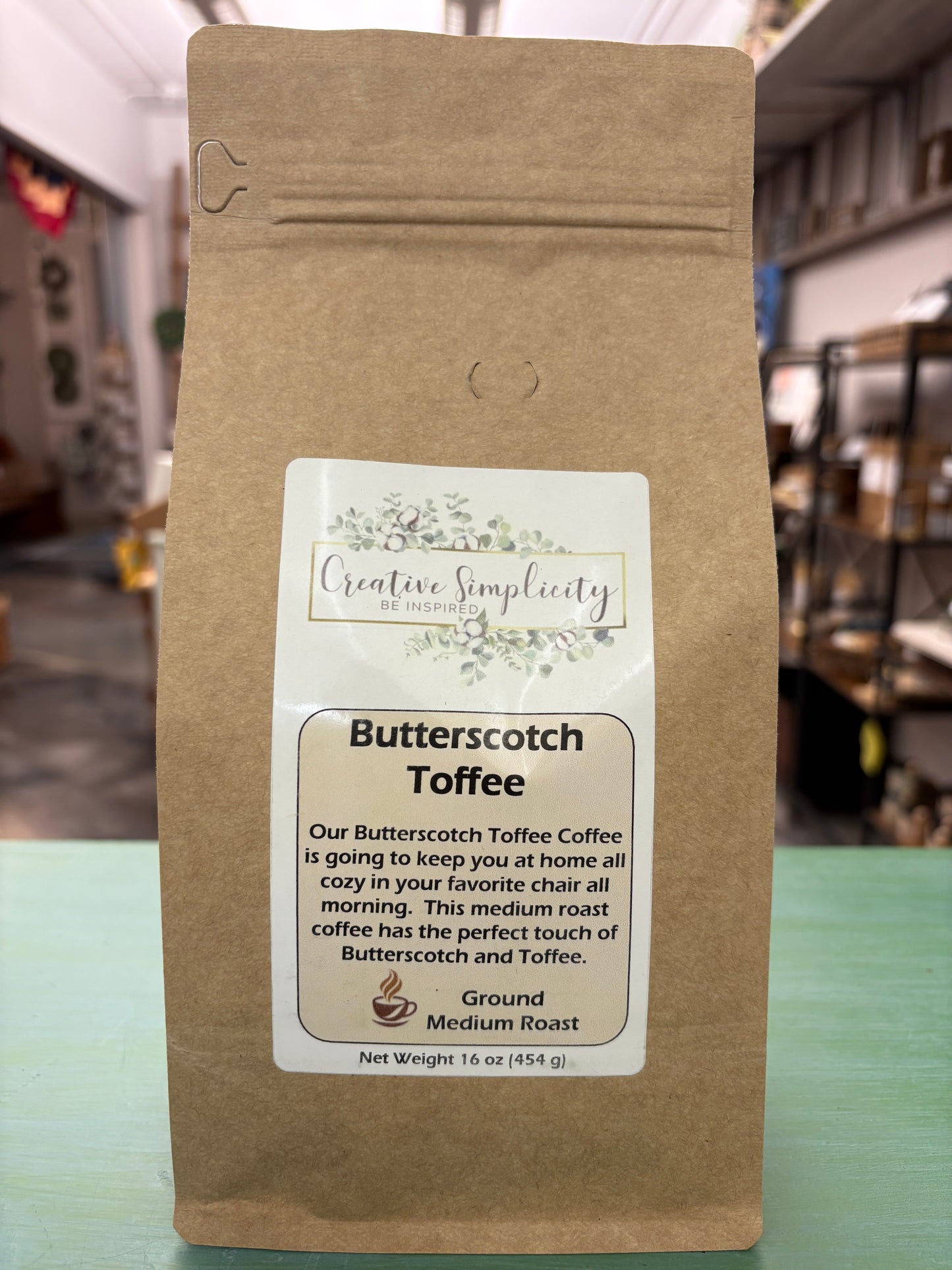 Brown coffee bag with a label stating Butterscotch Toffee Coffee on a blurred indoor background