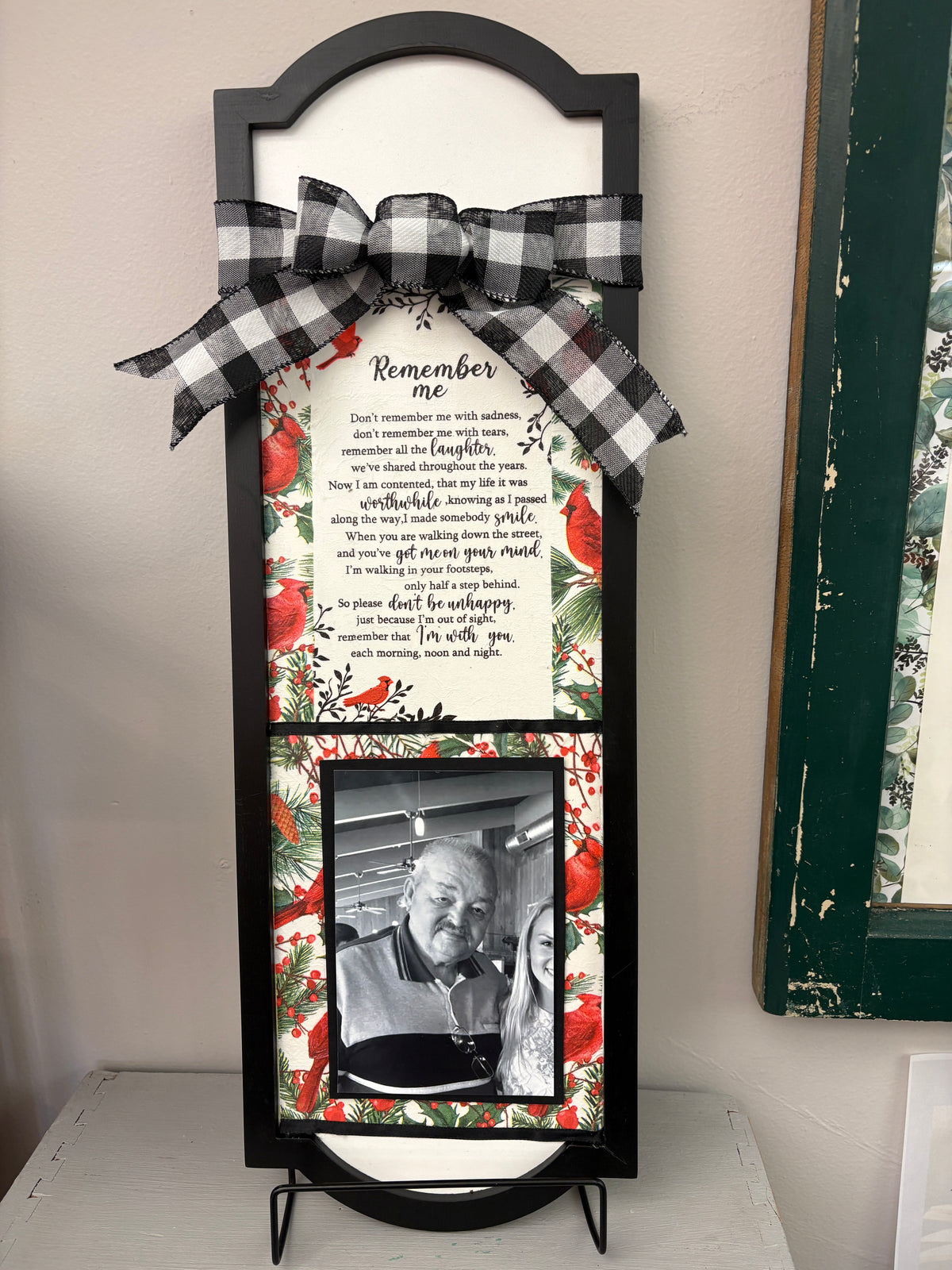 A black wooden double-photo frame with a bow and holiday-themed floral border, featuring a printed 'Remember me' poem on the upper section and a placeholder photo area for a second photo on the lower section.