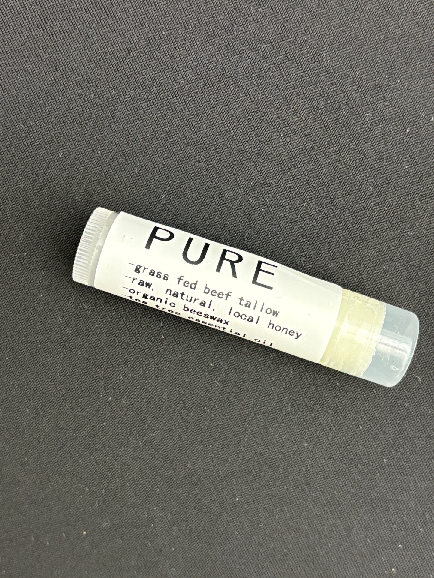 A stick of chapstick labeled 'PURE' with ingredients listed as 'grass-fed beef tallow, organic beeswax, natural beeswax', and 'local honey'.