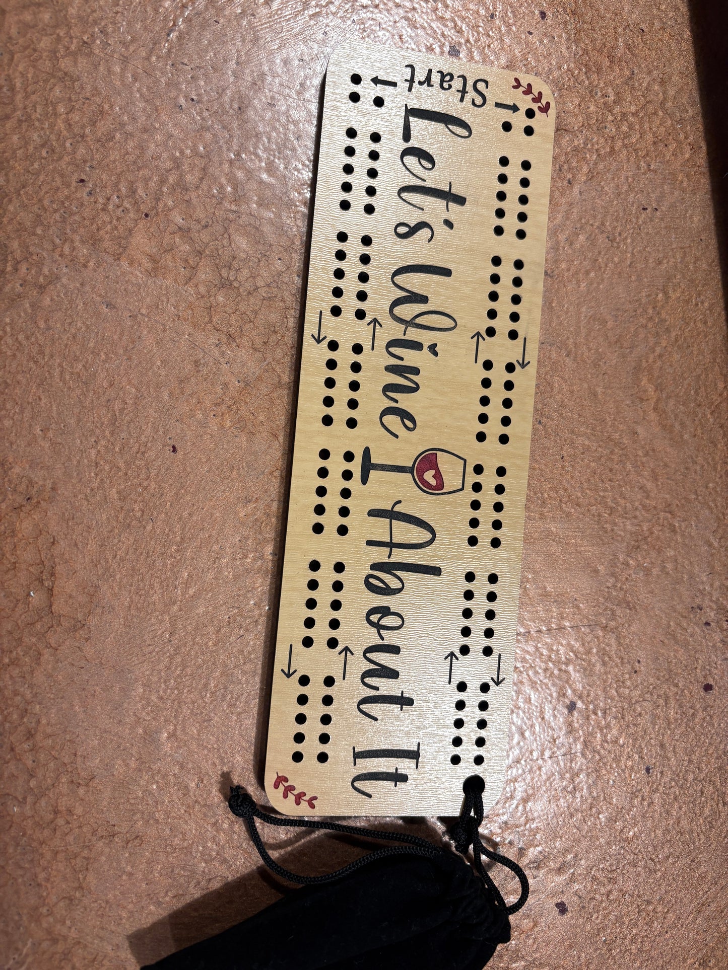 Wooden cribbage board with 'Let's Wine I About It' text on a brown surface