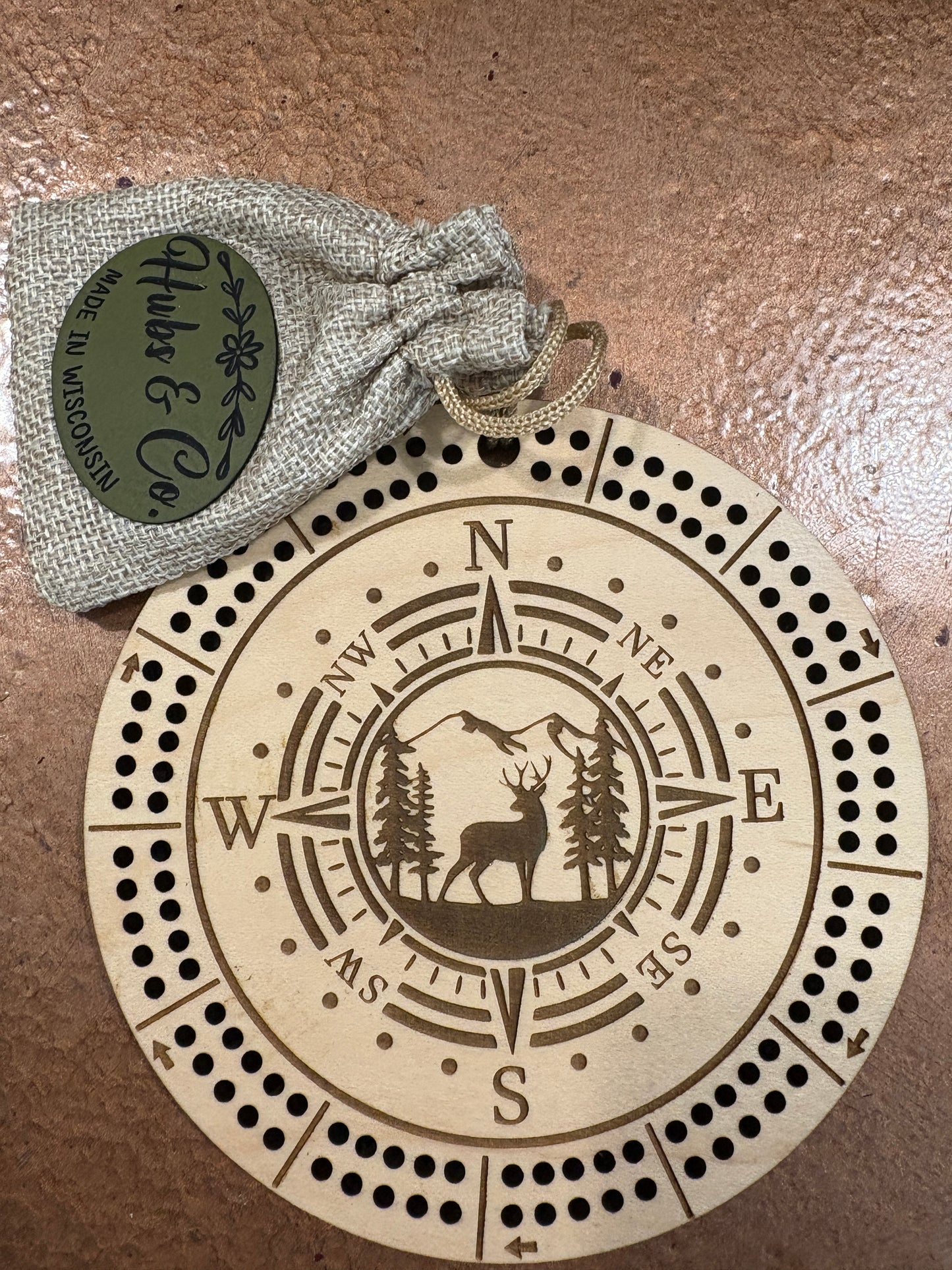 Wooden cribbage board with compass design and Huls & Co branded pouch on a brown surface