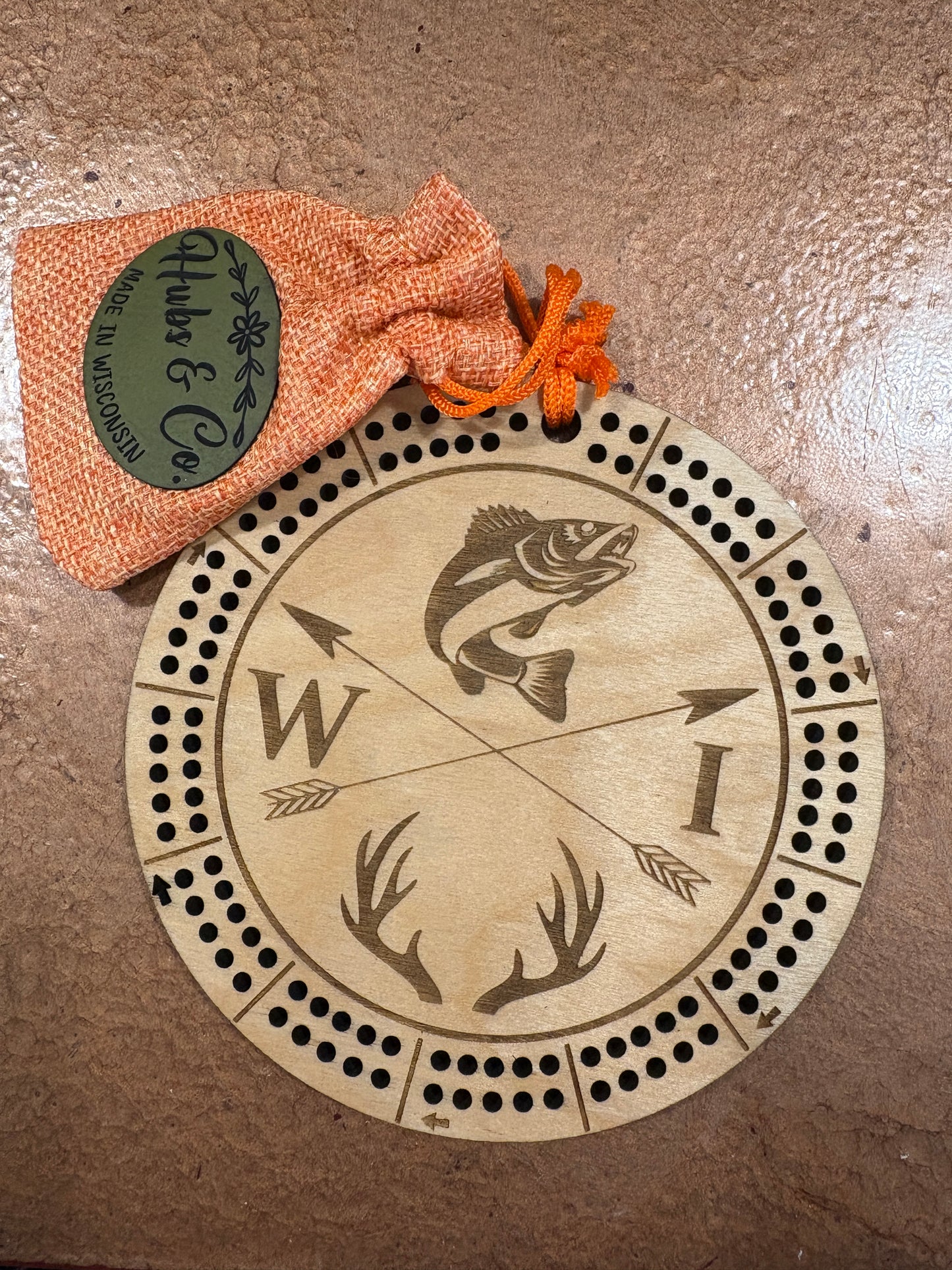 Wooden cribbage board with engraved designs on a textured surface, accompanied by a small drawstring bag.