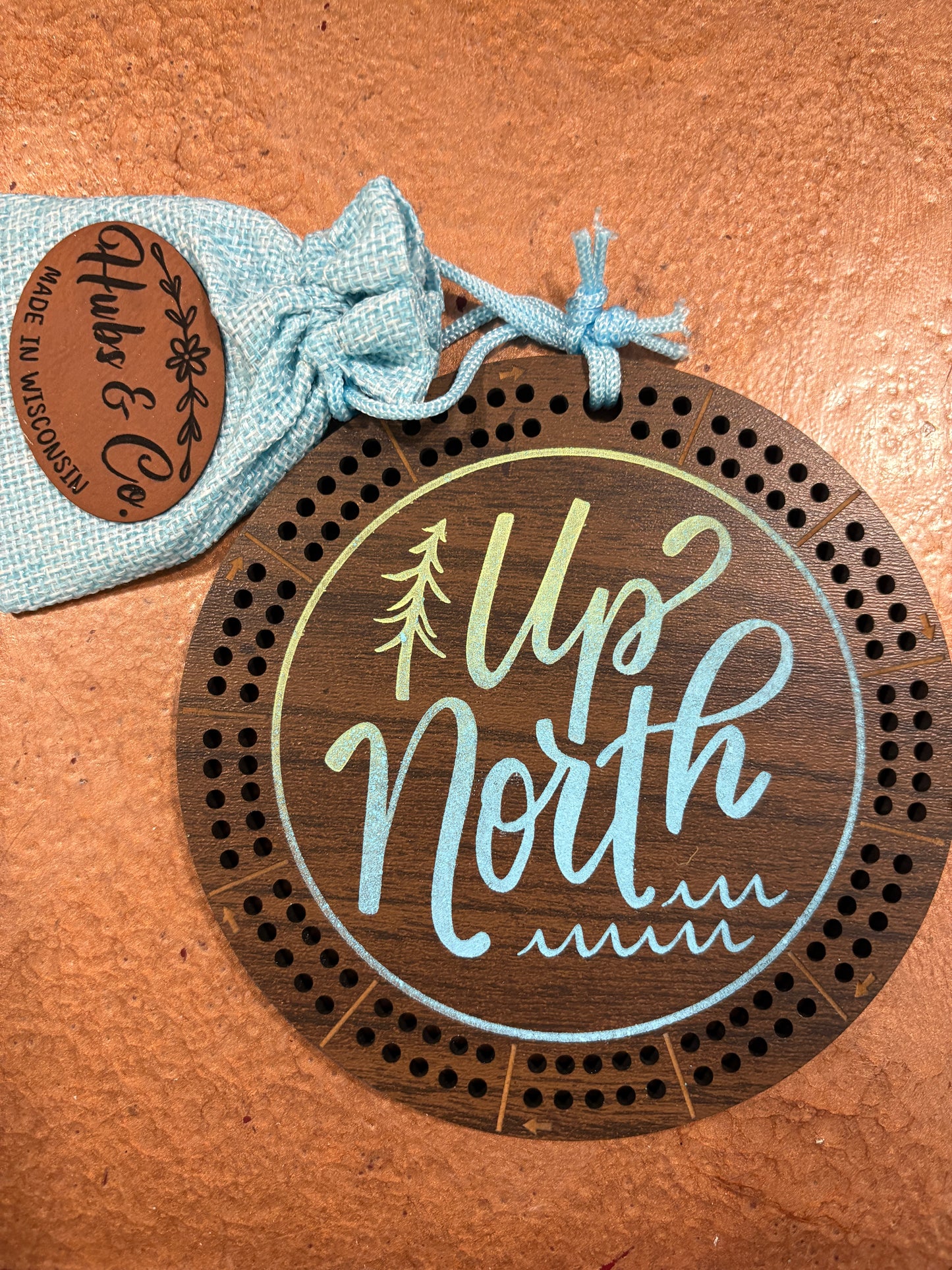 Wooden cribbage board with 'Up North' text and a small bag labeled 'Hubs & Co.' on a brown background
