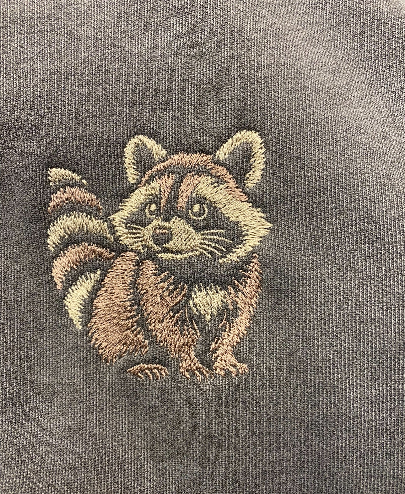 Embroidered raccoon design on a dark fabric background