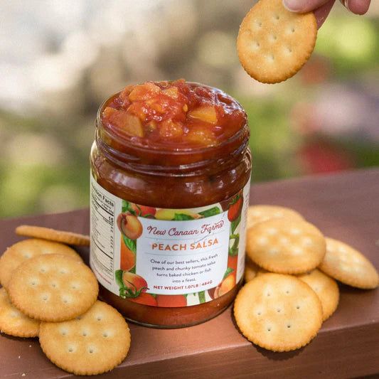 Jar of peach salsa with crackers on a wooden surface