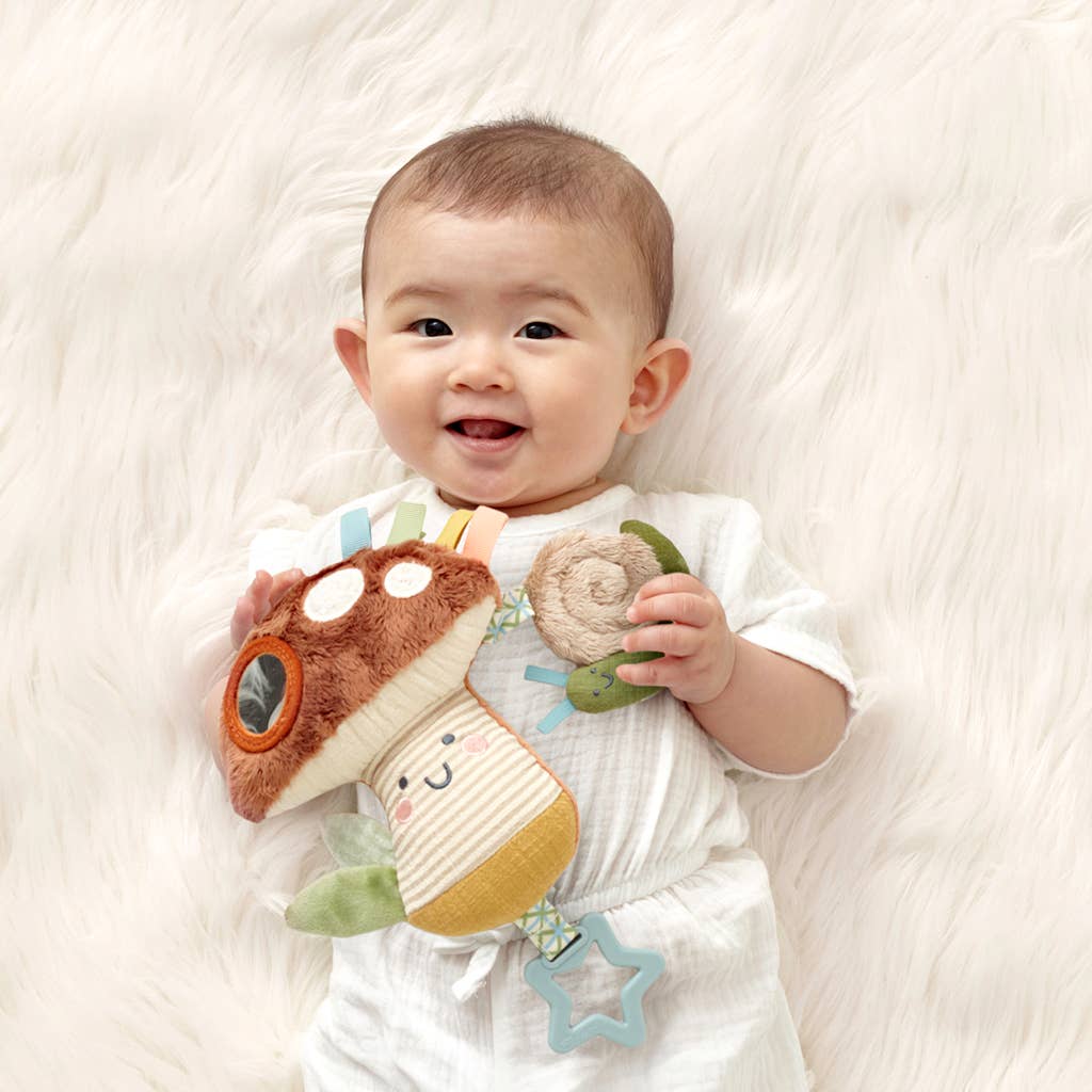 Baby holding a soft toy with a smile on a white blanket