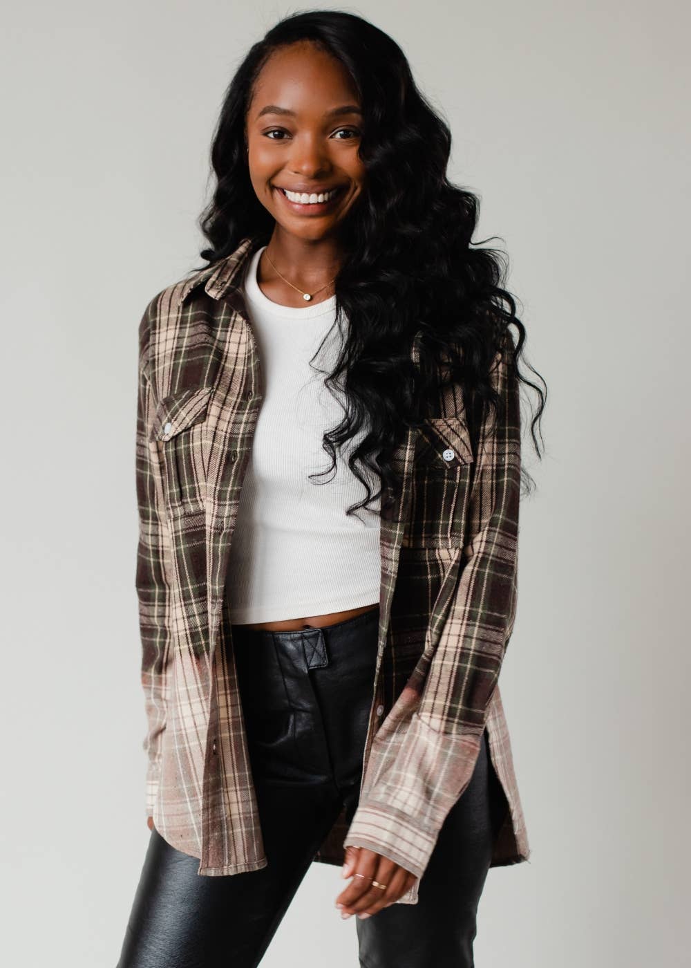 Woman wearing a plaid shirt over a white top and black pants on a plain background