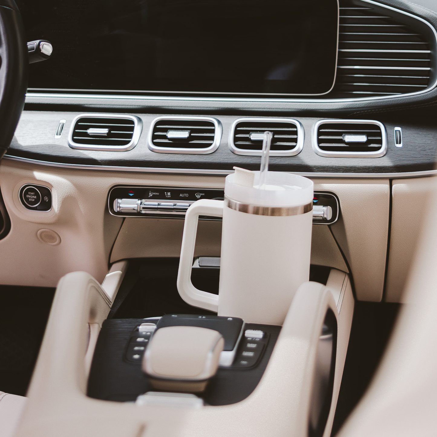 Car cup holder with a white mug and straw in a modern vehicle interior.