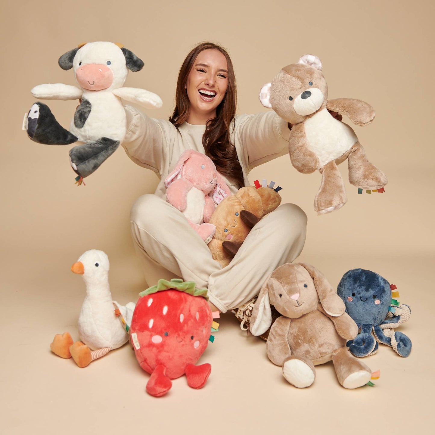 Woman holding and surrounded by various plush toys on a beige background