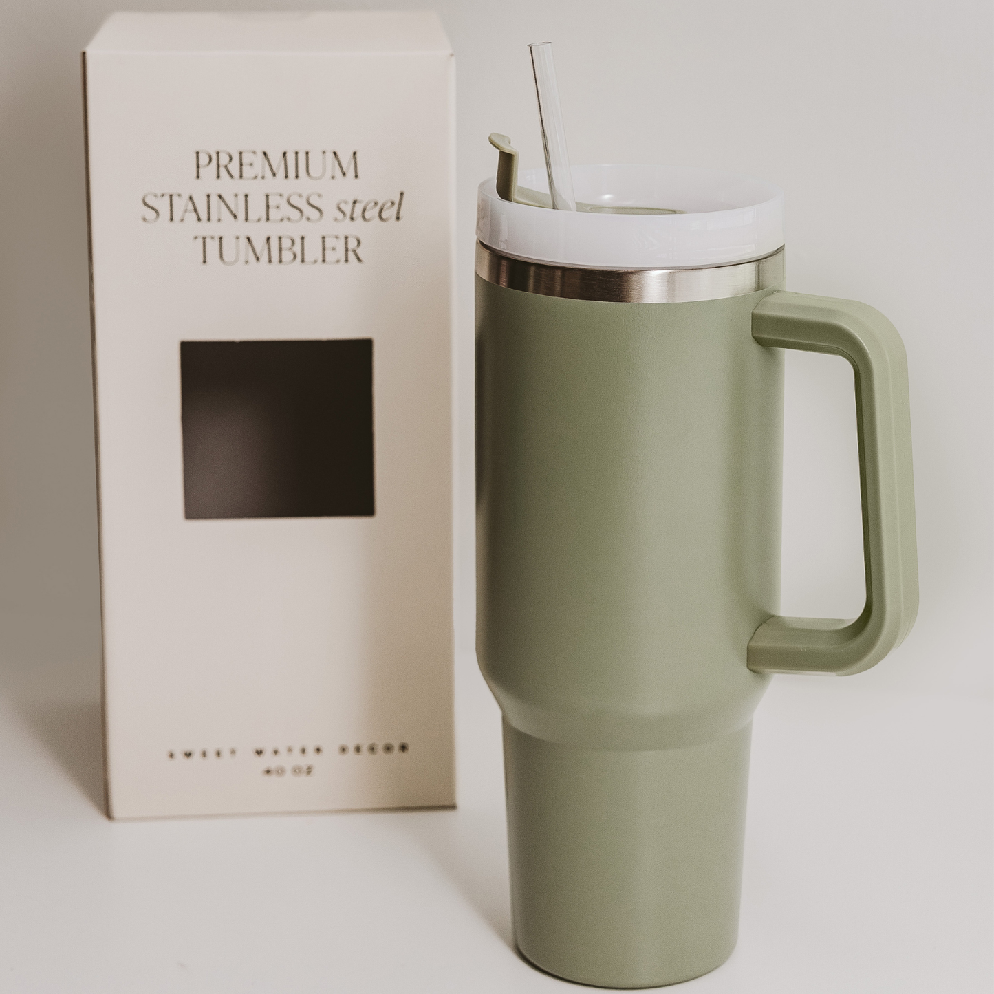 Green stainless steel tumbler with handle next to its packaging on a light background