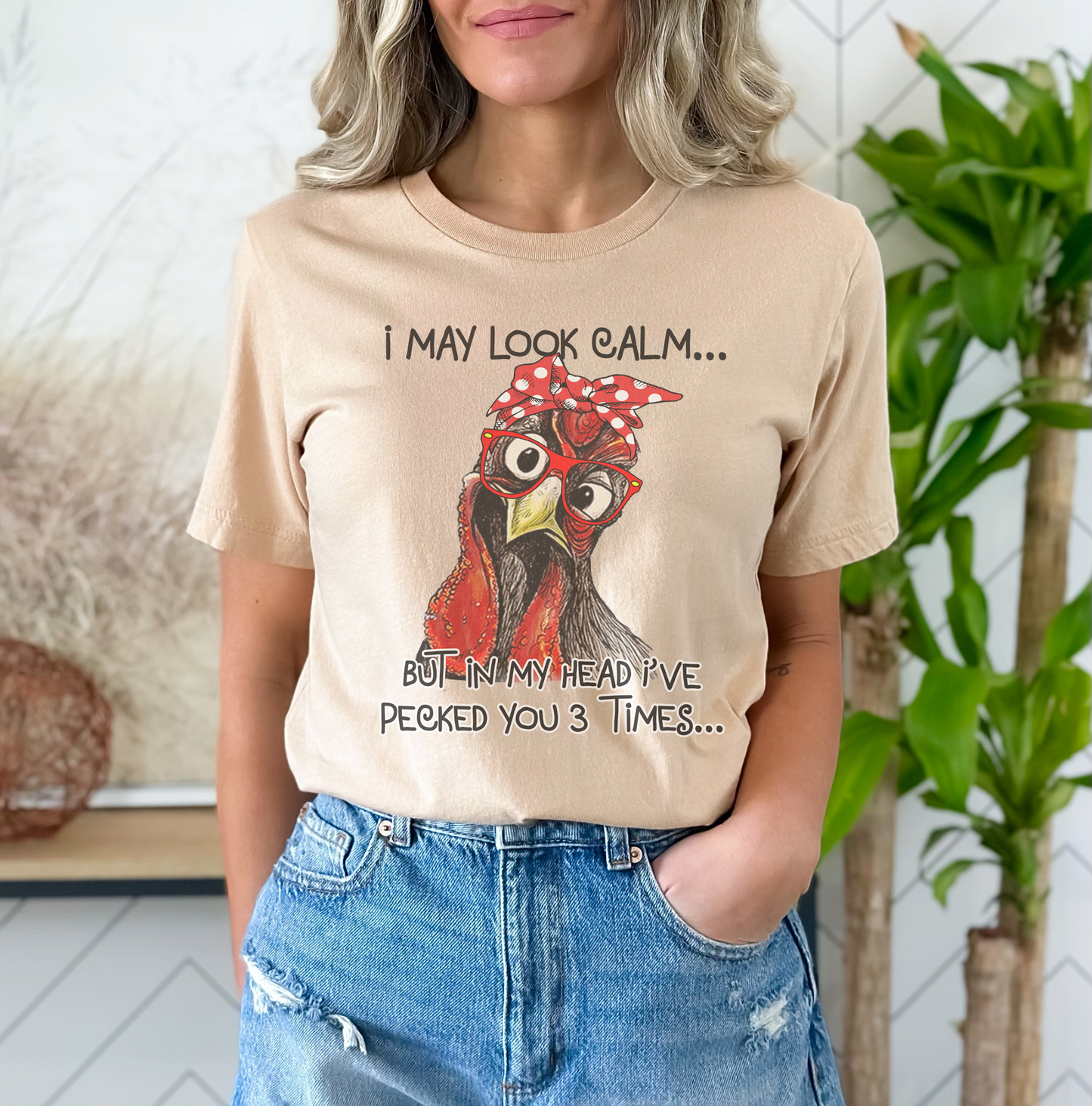Person wearing a beige t-shirt with a rooster graphic and text, standing indoors.