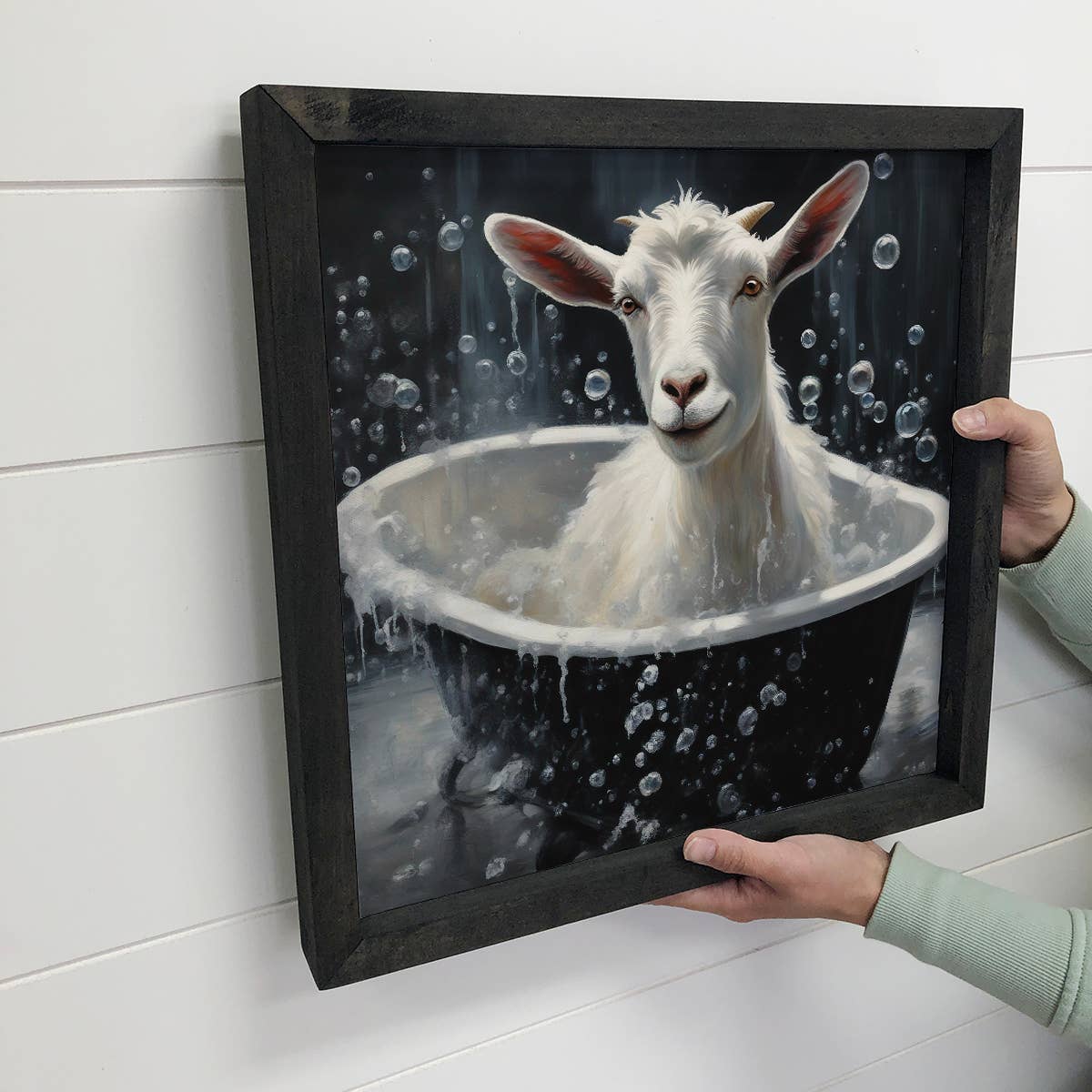 Framed artwork of a goat in a bathtub with bubbles on a white wall.