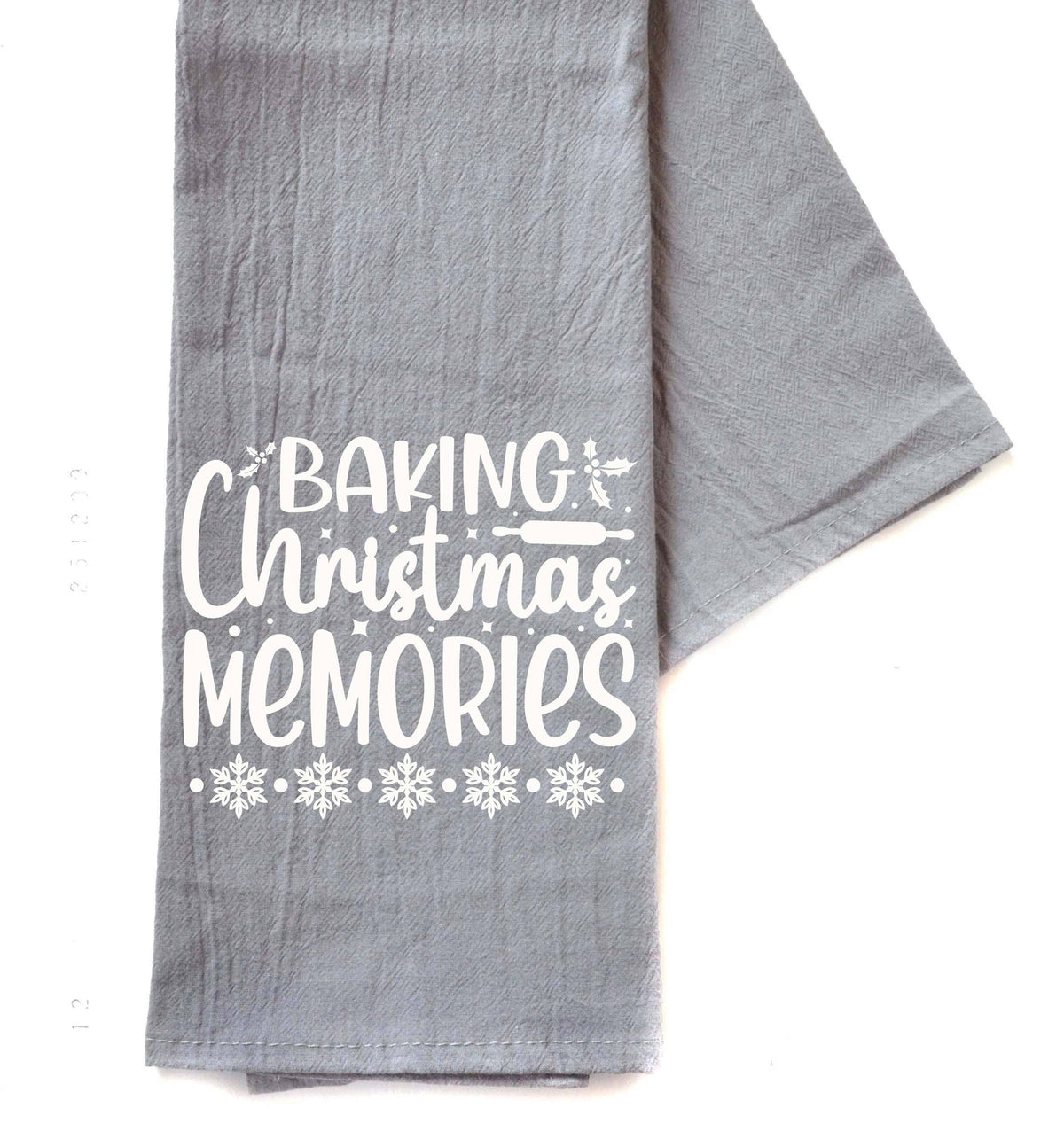 A gray kitchen tea towel with white printed text reading 'BAKING Christmas MEMORIES' and snowflake designs, laid flat on a white background.
