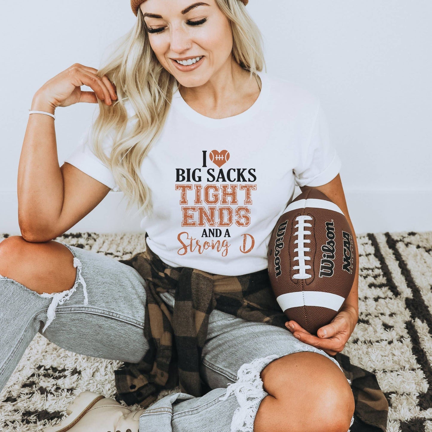Woman wearing a t-shirt with sports-themed text, holding a football on a patterned rug.