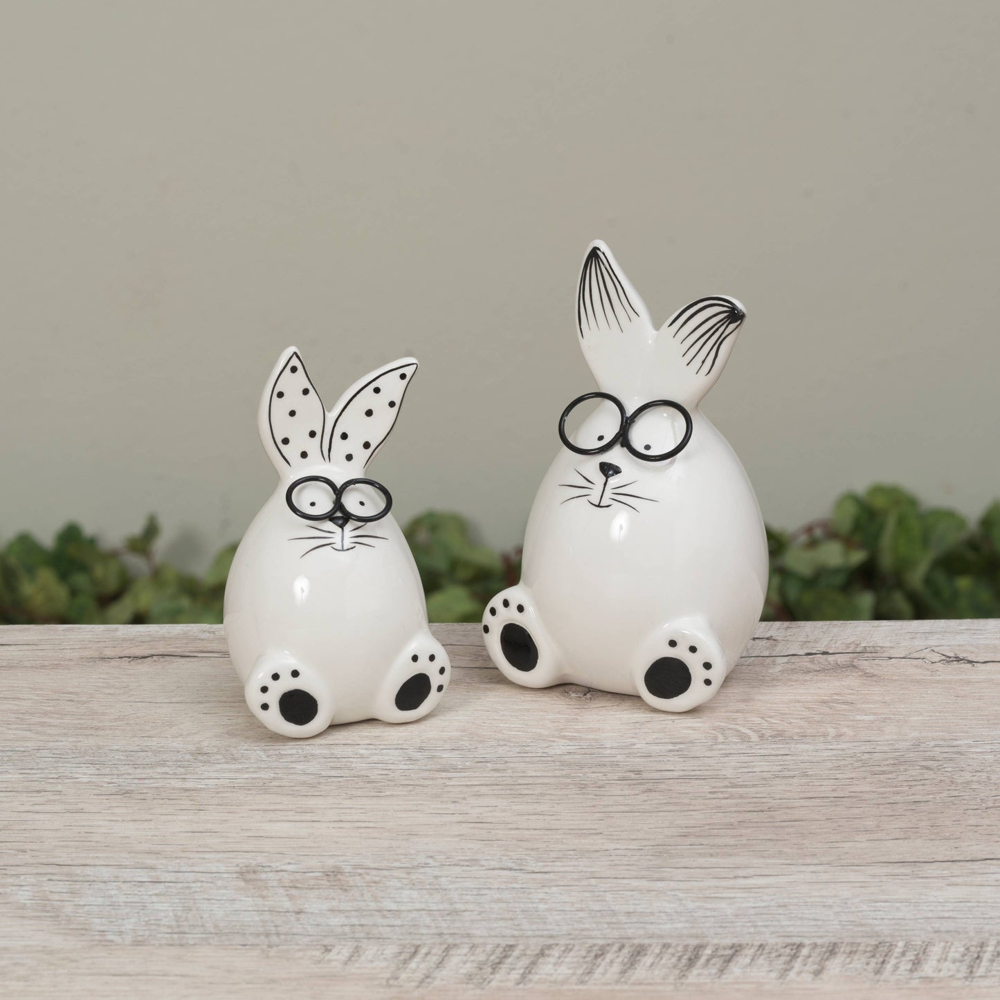 Two white ceramic rabbit figures with black glasses on a wooden surface.