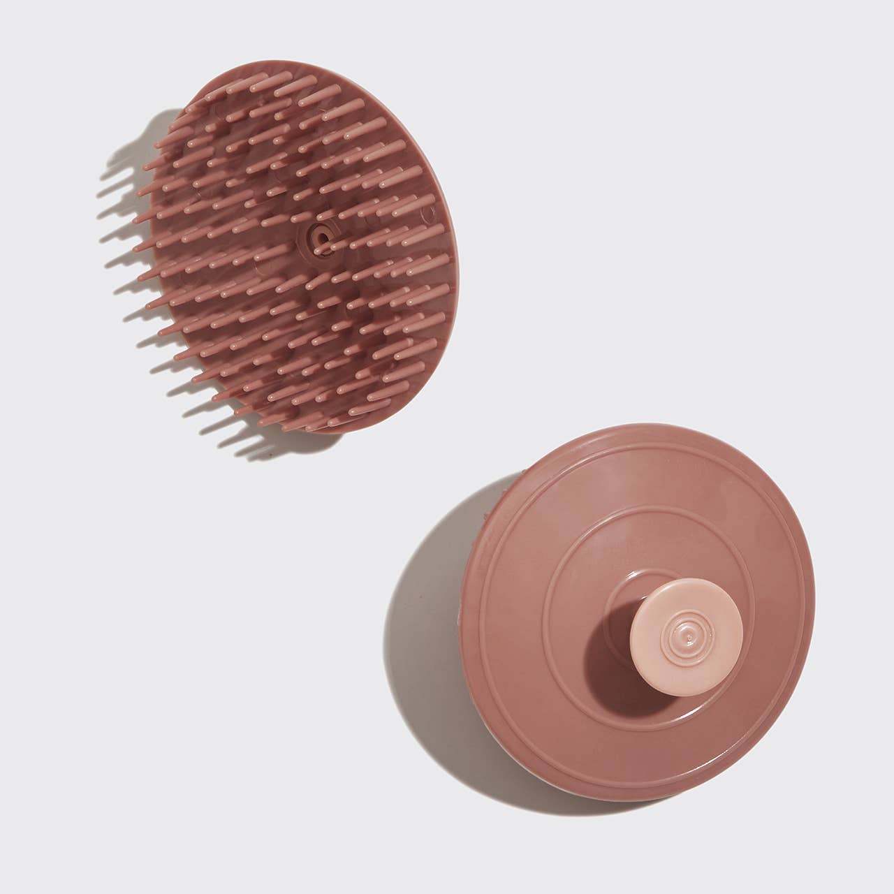 Round pink scrubber with bristle side and smooth side on a light gray background