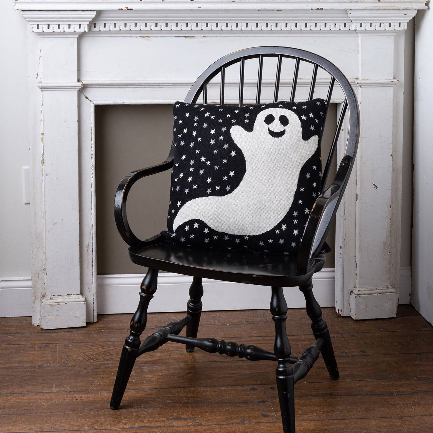 Black armchair with a pillow featuring a ghost design in front of a white fireplace.