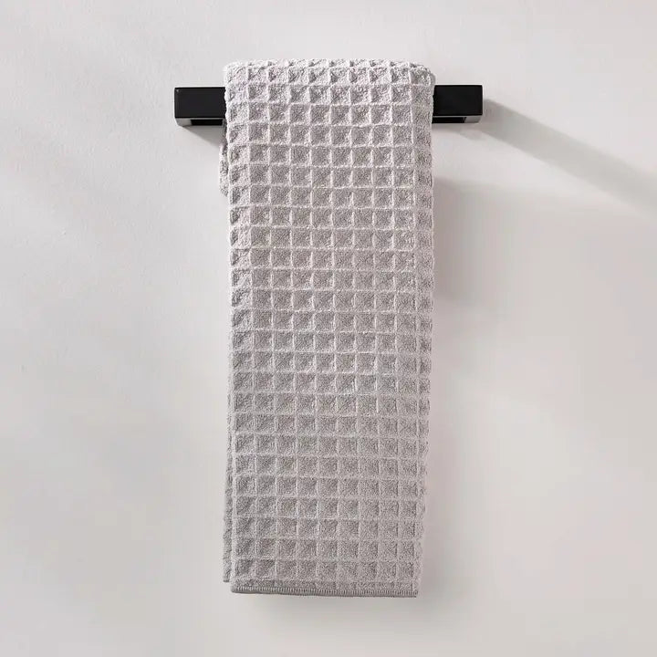 Light grey textured Geometry Waffle hand towel hanging on a black rod on a white wall